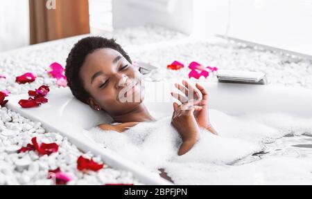 Femme afro-américaine prend bain avec mousse et pétales Banque D'Images