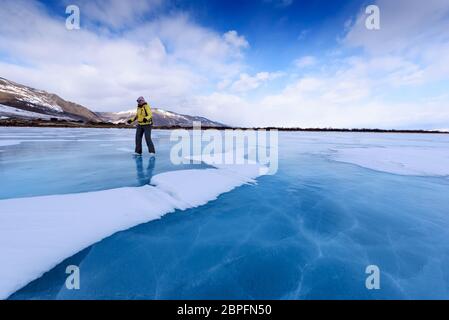 Une fille dans une veste jaune et des patins à glace se dresse sur le lac bleu du lac Baikal Banque D'Images