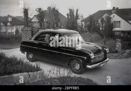 Années 1950, historique, dans une route de banlieue de grandes maisons semi-individuelles, un homme assis dans une voiture de l'époque dans son allée, Angleterre, Royaume-Uni. Banque D'Images