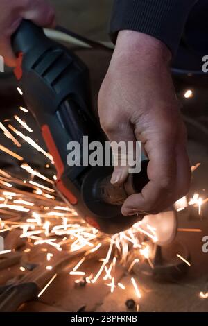 Vue avant des mains d'un homme travaillant sur une partie métallique d'un banc de jardin, utilisant une meuleuse électrique pendant que des étincelles volent dans le travail industriel Banque D'Images