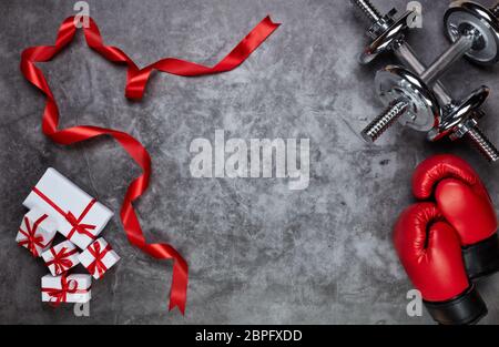 Haltères, gants de boxe, boîtes-cadeaux sur fond gris.vue du dessus avec espace de copie. Carte de Saint-Valentin. Concept de forme physique, de sport et de mode de vie sain. Banque D'Images