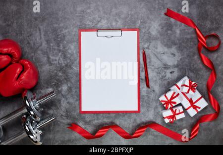 Haltères, gants de boxe, boîtes-cadeaux et tablette avec feuille vierge sur fond gris.vue du dessus. Carte de Saint-Valentin. Fitness, sport et santé Banque D'Images