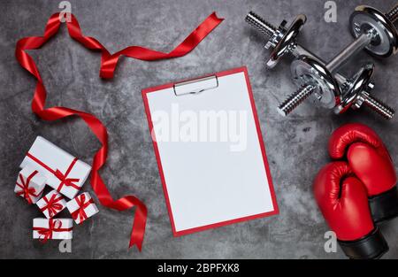 Haltères, gants de boxe, boîtes-cadeaux et tablette avec feuille vierge sur fond gris.vue du dessus. Carte de Saint-Valentin. Fitness, sport et santé Banque D'Images