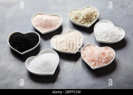 Variété de sels culinaires mondiales dans des bols en forme de coeur noir avec sel de Hawaï, sel de l'Indus, la Fleur de sel, Flor da Sal, Geurande rock salt, sel Banque D'Images