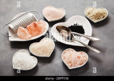 Un assortiment de sels culinaires naturels du monde entier sur des plats en forme de coeur noir avec sel de Hawaï, sel de l'Indus, la Fleur de sel, Flor da Sal, Geu Banque D'Images