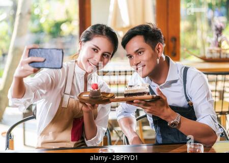 Couple asiatique deux partenaires de la petite entreprise propriétaire de prendre selfie et de présenter la boulangerie dans le café-restaurant quand recrile vlog, gâteau et dessert, entrepren Banque D'Images