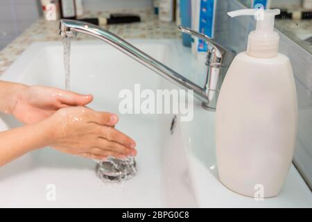 L'enfant se lave les mains sous le robinet, à l'avant-plan d'un tube de savon liquide Banque D'Images