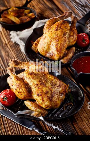 Deux poulets rôtis ou poussin printemps servi sur les poêlons avec un côté plat de tomates et les quartiers de pommes de terre Banque D'Images