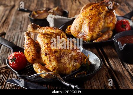 Deux des rôties ou poussin printemps poulets sur poêlons avec tomates sur une table rustique bois brut Banque D'Images