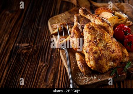 Jeune poussin grillé ou au printemps de poulet marinés dans une sauce épicée et servi avec les quartiers de pommes de terre et de tomate sur une vieille planche sur une table en bois avec cop Banque D'Images