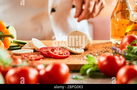 Chef de la préparation d'une salade caprese en saupoudrant l'de tranches de tomate et de mozzarella avec du sel et d'épices sur une planche en bois Banque D'Images