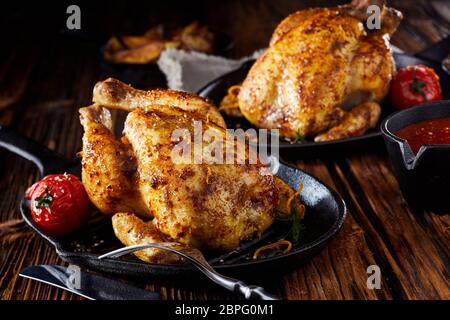 Deux petits poulets rôtis ou poussin printemps noir sur poêlons servi avec des tomates sur une table en bois rustique Banque D'Images