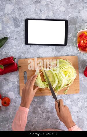 La main de femme Chou coupe près de la tablette numérique avec écran blanc sur le comptoir de la cuisine Banque D'Images