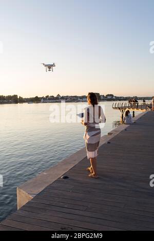 Une photographe française pilote de drone se tient sur le quai d'Etel et récupère son drone après une séance de photographie au coucher du soleil. Etel. Bretagne. Banque D'Images