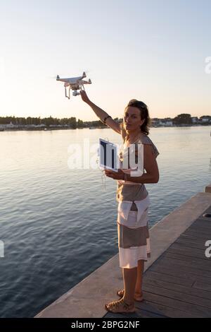 Une photographe française pilote de drone se tient sur le quai d'Etel et récupère son drone après une séance de photographie au coucher du soleil. Etel. Bretagne. Banque D'Images