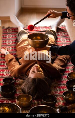 Femme faisant massage relaxant, méditation, thérapie sonore avec des bols de chant tibétien. Soulagement de stress. Mise au point sélective. Vue de dessus. Banque D'Images