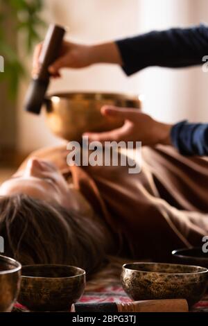 Femme faisant massage relaxant, méditation, thérapie sonore avec des bols de chant tibétien. Soulagement de stress. Mise au point sélective sur le bol. Vue de dessous. Banque D'Images