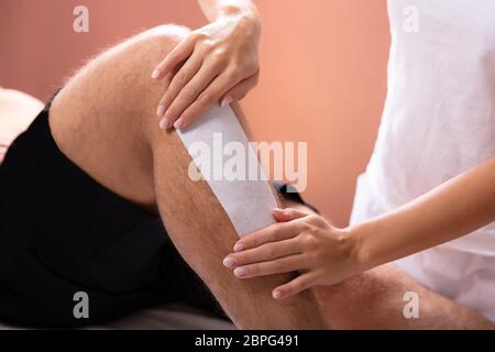 Close-up de la thérapeute de l'homme Epilation jambe avec bande de cire Banque D'Images