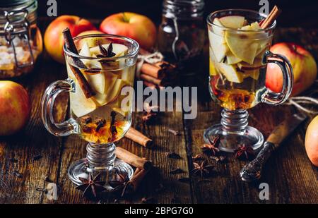 Deux verres de boisson chaud Apple avec girofle, cannelle, étoile d'anis et de sucre candy. Tous les ingrédients et quelques ustensiles de cuisine sur table en bois. Banque D'Images