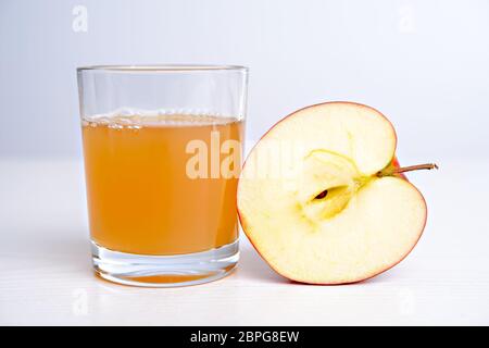 La moitié de pomme avec verre de jus naturellement nuageux in front of white background Banque D'Images