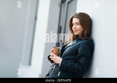 Jeune fille jolie debout près du mur avec une tasse de café Banque D'Images