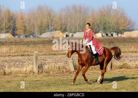 HORTOBAGY, HONGRIE, NOVEMBRE 04. 2018: Femme hongroise csikos en costume traditionnel folklorique à cheval son cheval entraîné. Novembre 04. 2018, Hortobagy, Hun Banque D'Images