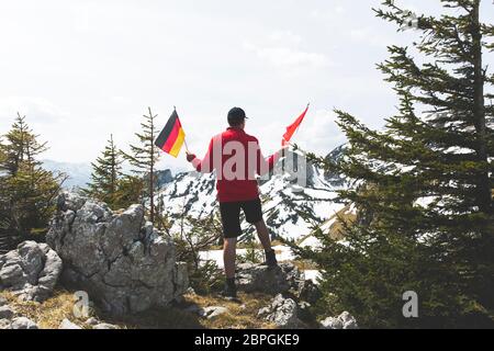 Male hiker avec pull rouge est maintenant un drapeau allemand dans les montagnes Banque D'Images