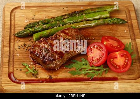 Près d'un steak de bœuf rôti grillé aux asperges vertes et tomates cerises sur planche à découper en bois, high angle view Banque D'Images