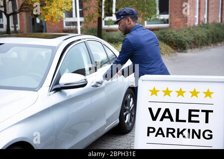 Heureux homme d'ouverture de porte de voiture près de voiturier Voiturier Sign Banque D'Images