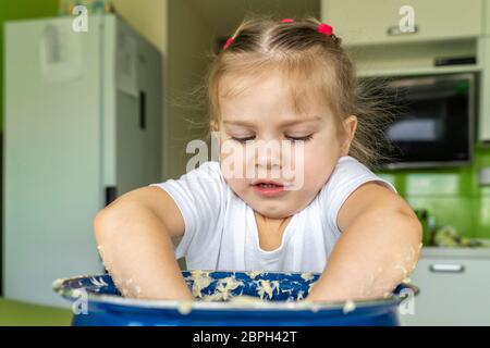 petite fille de 3-4 ans joue avec la pâte dans une grande casserole bleue dans la cuisine. activités avec les enfants sur l'auto-isolation Banque D'Images