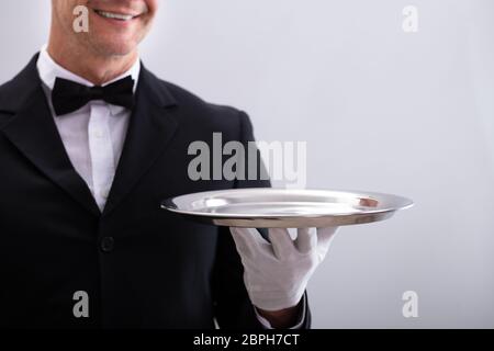 Close-up of Waiter's Hand Holding Empty Silver Tray Against White Background Banque D'Images