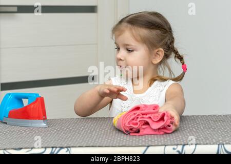 une jolie petite fille joue une femme au foyer, repassant les vêtements des enfants avec un fer à repasser. auto-isolation et quarantaine avec les jeunes enfants Banque D'Images