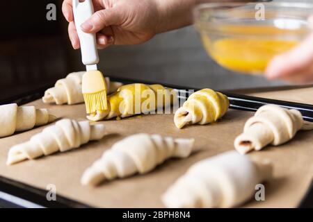 Faire cuire des croissants à la maison et couvrir la pâte avec du jaune d'œuf à l'aide d'une brosse à pâtisserie. Banque D'Images