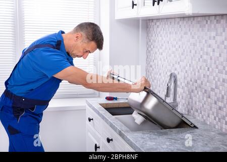 Photo de mâle mature Workman fixant un évier de cuisine Banque D'Images