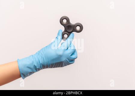 Vue latérale du profil de la main humaine en gants chirurgicaux bleus tenant un spinner de violon noir. Vue en studio, à l'intérieur, isolée sur fond gris. Banque D'Images