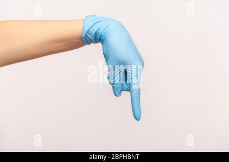 Vue latérale du profil gros plan de la main humaine avec des gants chirurgicaux bleus montrant ou pointant vers le bas avec le doigt. Vue en salle, en studio, isolée sur fond gris Banque D'Images