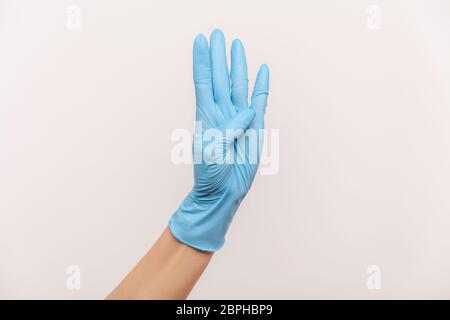 Vue latérale du profil gros plan de la main humaine avec des gants chirurgicaux bleus, portant le numéro quatre 4 avec la main. Vue en studio, à l'intérieur, isolée sur fond gris. Banque D'Images