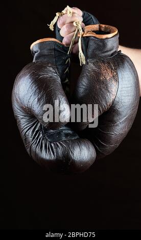 Part détient une paire de vieux gants de boxe en cuir brun, fond noir Banque D'Images