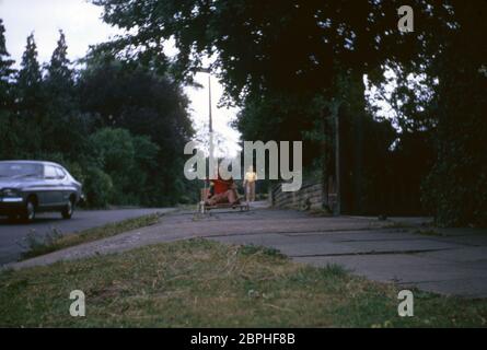 Une maman marchant après ses enfants sur la route en parcourant leur kart maison le long du pavé dans la banlieue, Hatch End Park Estate, Milne Feild, Hatch End, Middlesex, Royaume-Uni Banque D'Images