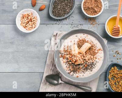 Du jour au lendemain de l'avoine dans un bol et les ingrédients - la banane, CVL, amandes et noix, amandes, miel et pollen gris sur fond de table en bois. Petit-déjeuner sain d'avoine Banque D'Images