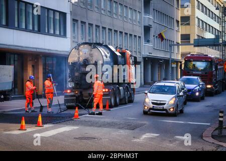 L'équipe de Street Works répare les vieux pavés d'asphalte de la ville. Des hommes au travail, la circulation avec des voitures et un camion passant. Helsinki, Finlande. 13 mai 2020. Banque D'Images