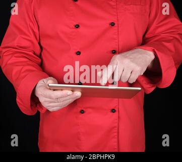 Chef en uniforme rouge tenant une tablette électronique dans ses mains et de toucher l'écran, fond noir Banque D'Images