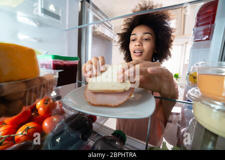 Femme de la faim en tenant la plaque sandwich de jambon frais dans le réfrigérateur Banque D'Images