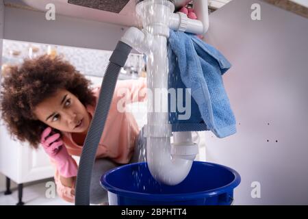 Close-up of a young woman inquiets appelant plombier pour réparer une fuite du tuyau de l'évier dans la cuisine Banque D'Images