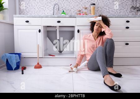 Déçu African Woman Broken pipe lavabo dans la main assis sur le plancher de la cuisine Banque D'Images