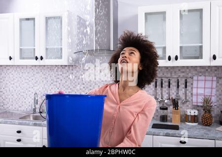 Close-up d'une jeune femme inquiète la collecte de l'eau qui coulait du plafond dans le seau bleu Banque D'Images