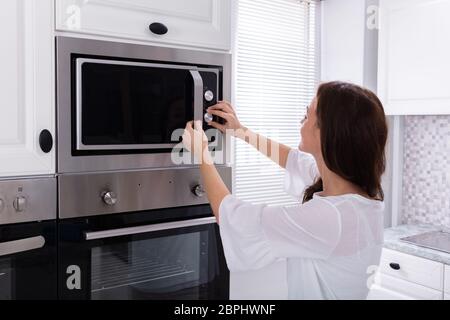 Vue latérale d'une jeune femme à l'aide d'un four micro-ondes four dans la cuisine Banque D'Images