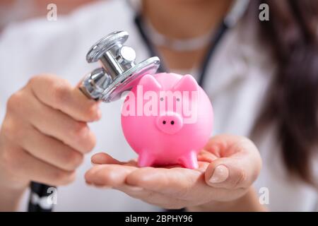 Close-up of main du médecin examinant Pink Piggybank with Stethoscope Banque D'Images