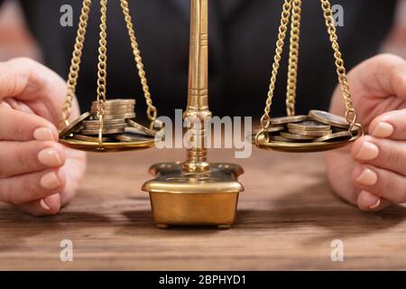 Close-up of a person's Hand protégeant les pièces sur l'échelle de la Justice sur le bureau en bois Banque D'Images