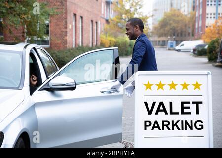 Heureux homme d'ouverture de porte de voiture près de voiturier Voiturier Sign Banque D'Images